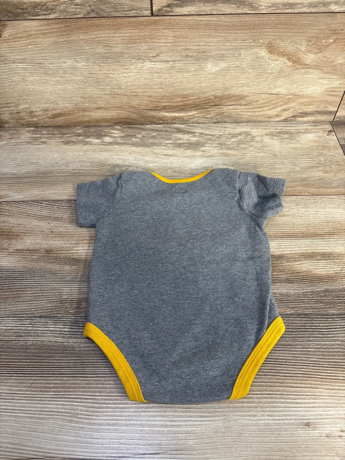 Back view of a grey John Deere baby bodysuit with yellow trim on a wooden background.