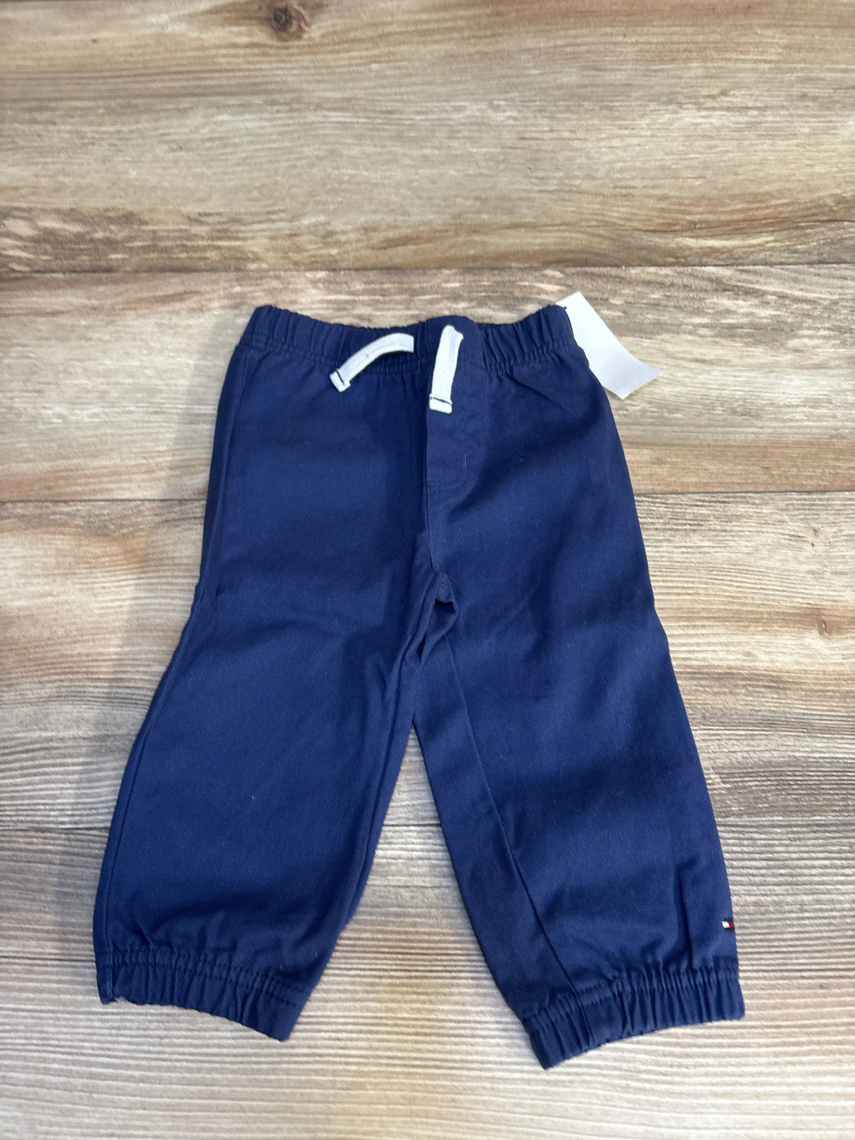 Navy blue kids joggers with white drawstring, elastic waist and cuffs, laid on wood floor