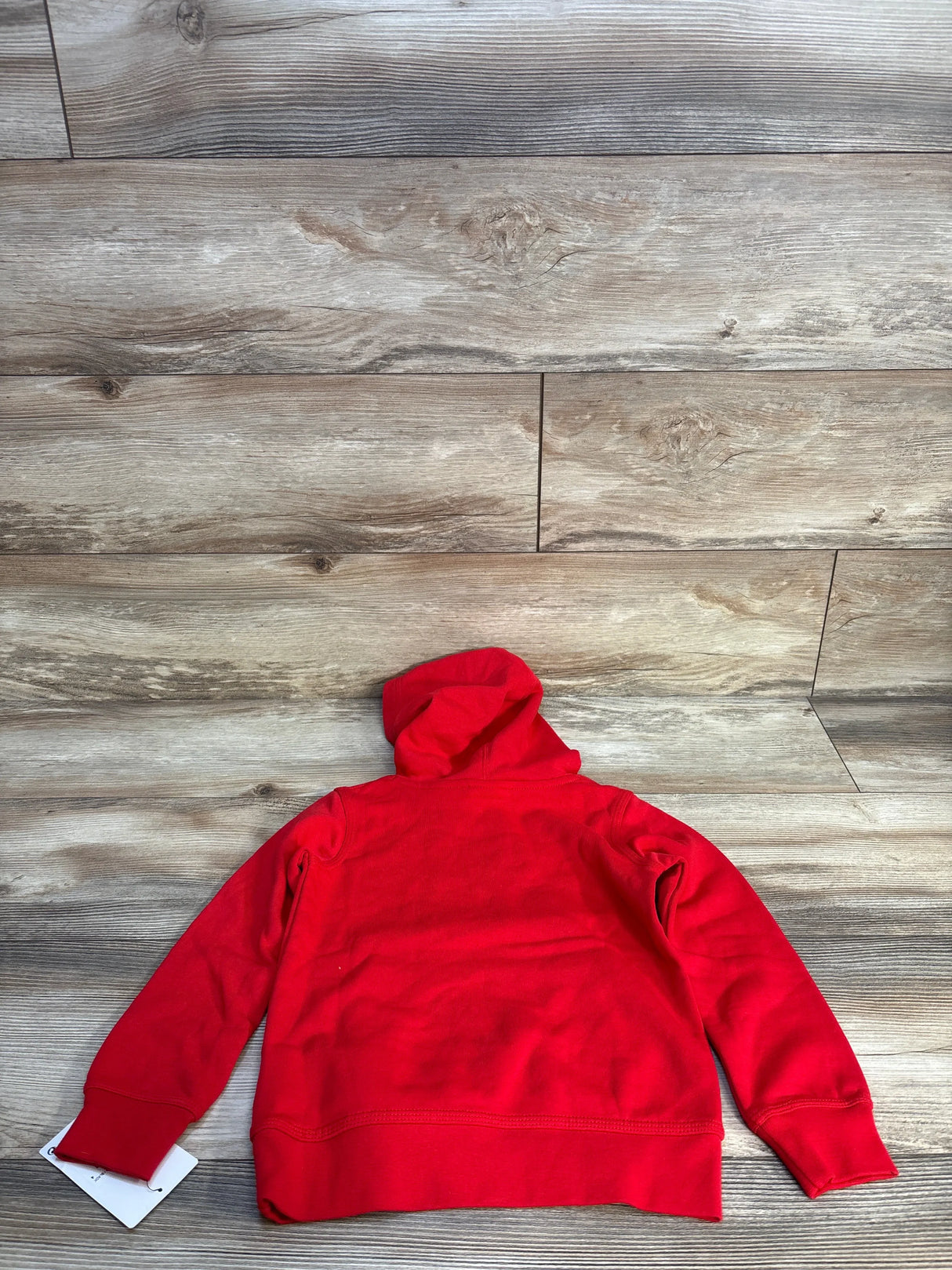 Red kids hoodie with long sleeves and hood laid flat on wood background
