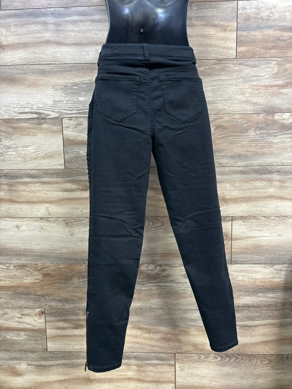 Black high-waisted skinny jeans with back pockets on mannequin, wood background
