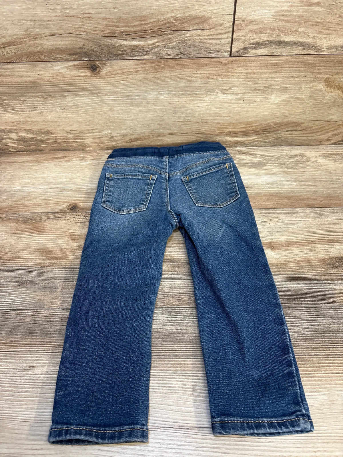 Kids blue denim jeans with elastic waistband, laid on wooden floor