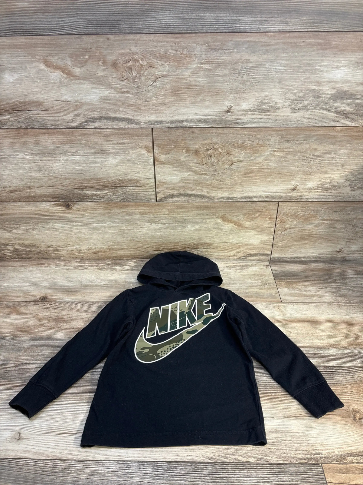 Black kids Nike hoodie with camo logo, long sleeves, displayed on wooden floor