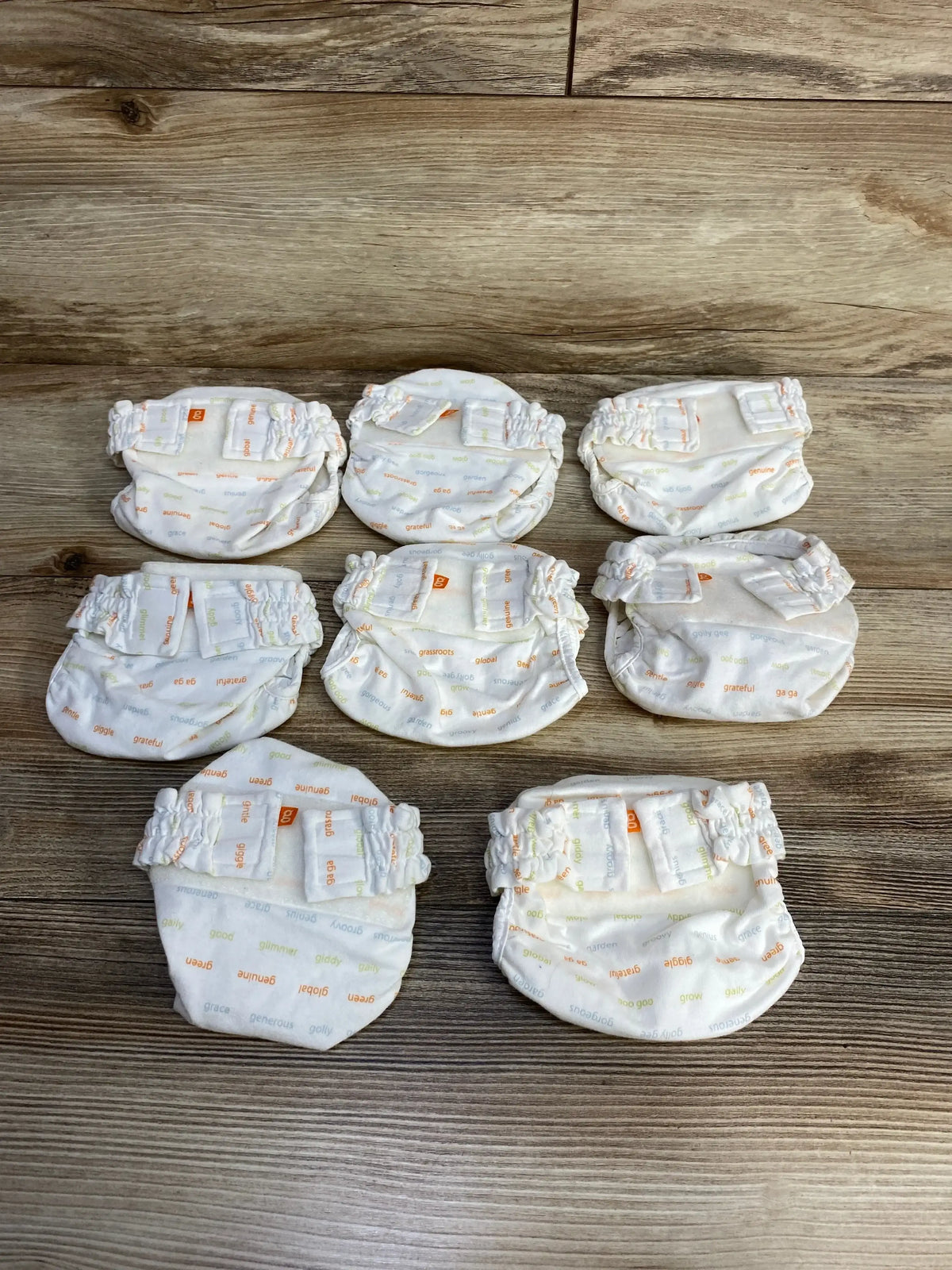 Front view of gDiapers newborn cloth diapers 8-pack showcasing ivory fabric with small word-print pattern on a white background