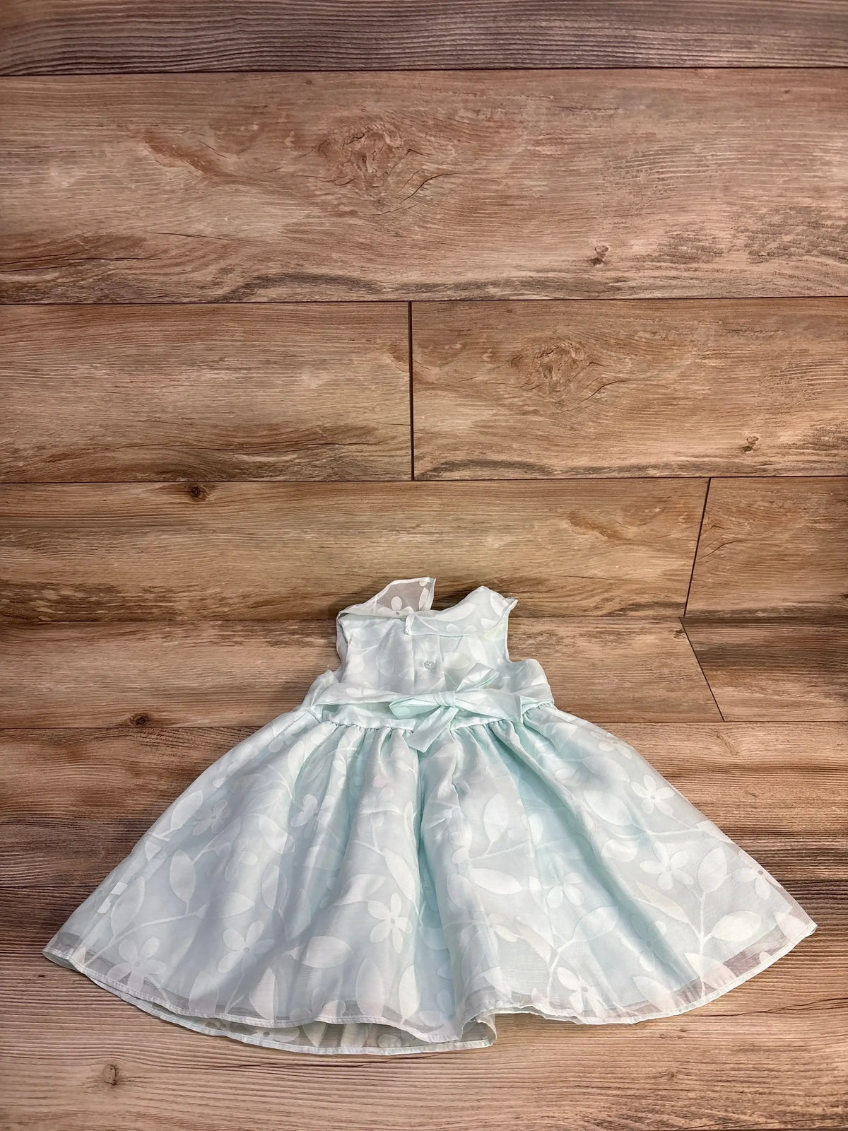 Light blue floral sleeveless girls dress with satin bow on wood background
