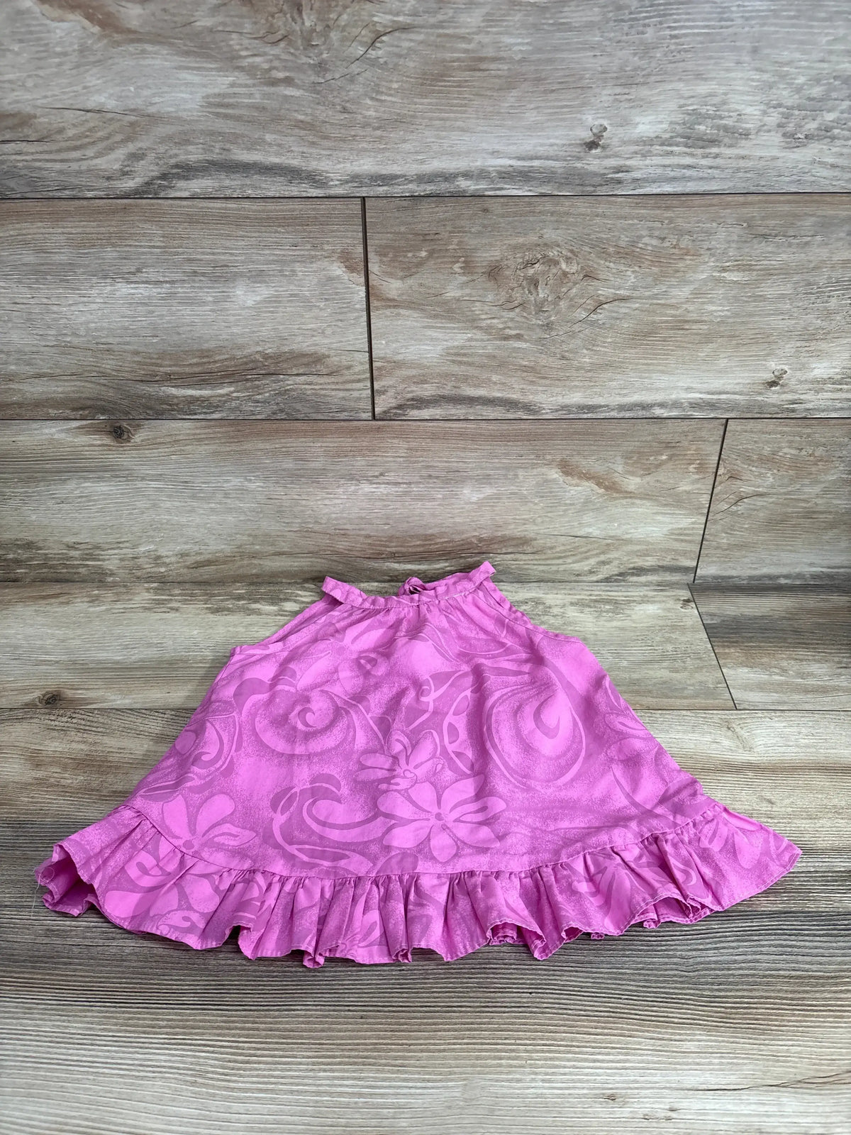 Top-down view of toddler pink floral halter dress (24 months) showing ruffled hem and swirled floral pattern on wood floor