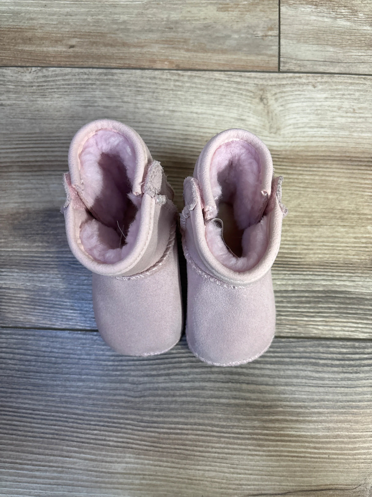 Top-down view of baby UGG Classic Soft Sole boots in pink showing plush shearling lining and suede exterior on light wood floor
