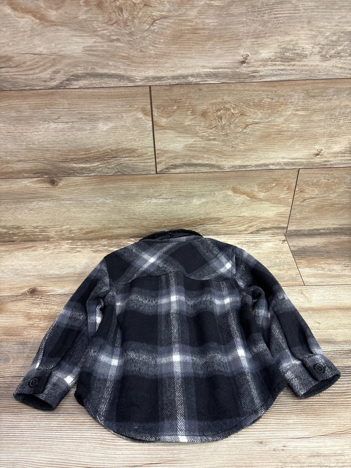 Back view of George plaid fleece button-up jacket showcasing black and gray plaid fleece fabric and buttoned cuffs on a wood floor
