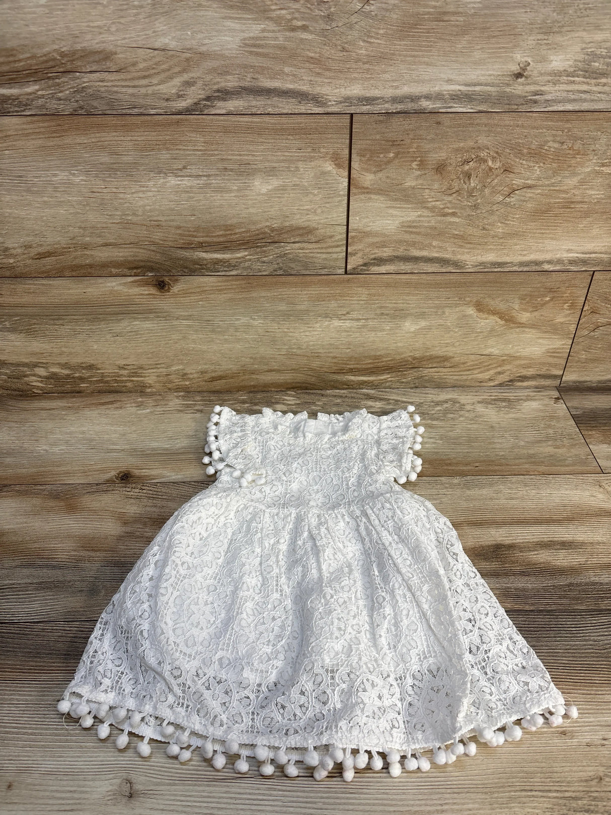 White lace baby dress with pom pom trim on wooden background
