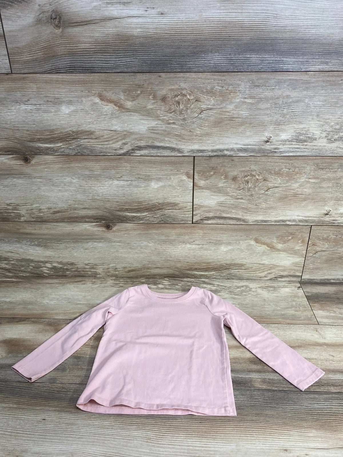 Front flat lay of Jumping Beans 3T long-sleeve pink toddler shirt showcasing crew neck and straight hem on wooden floor background