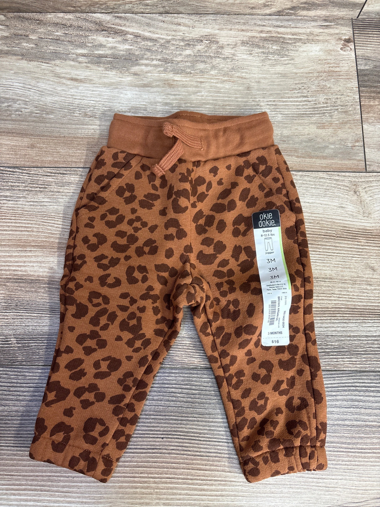 Okie Dokie baby jogger pants with brown leopard print for 3 months old, $16, on wooden floor