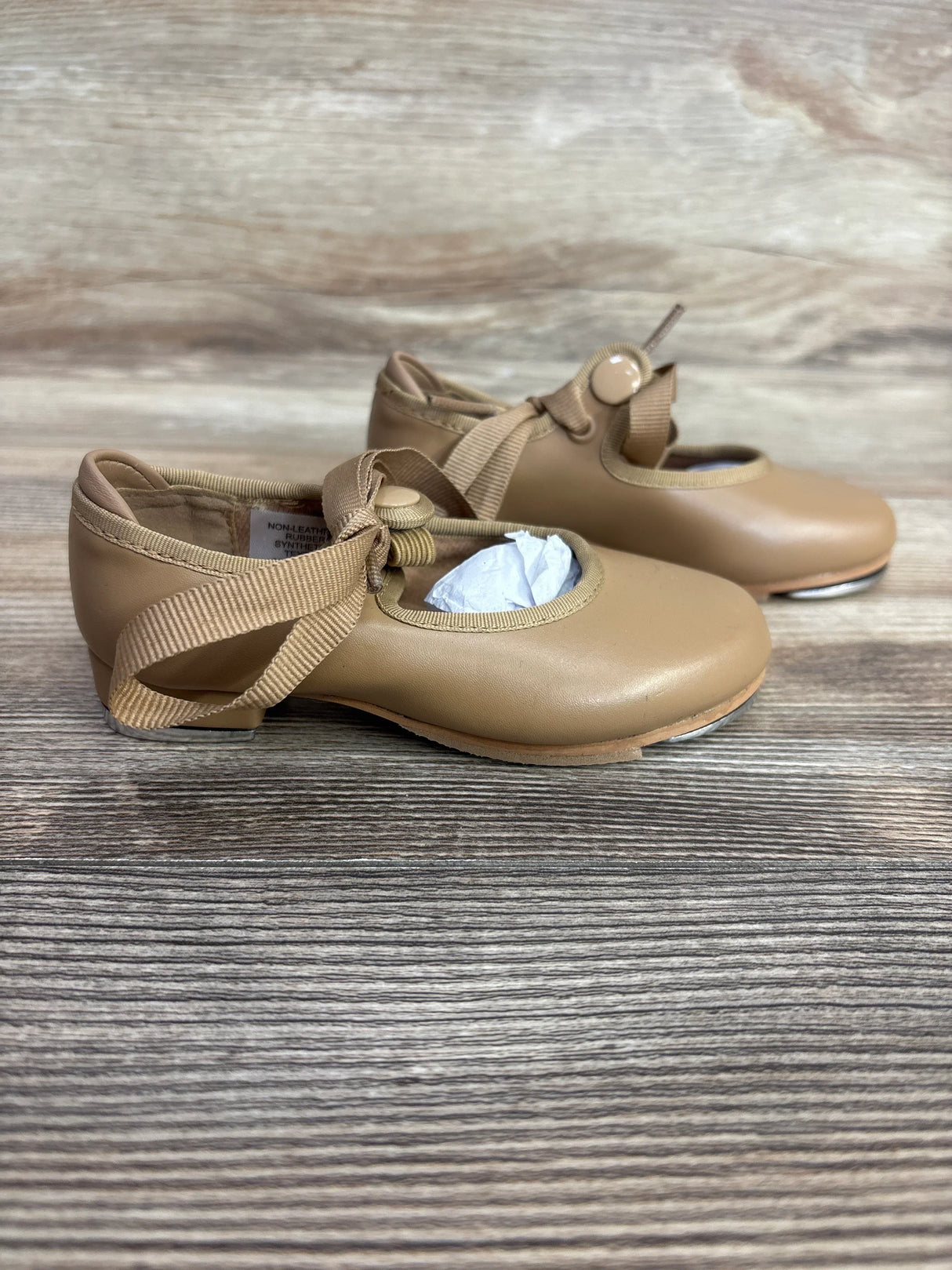 Side view of Bloch Annie Tyette tap shoes in tan, size 6.5C showcasing ribbon strap with button closure and metal heel taps on wood floor