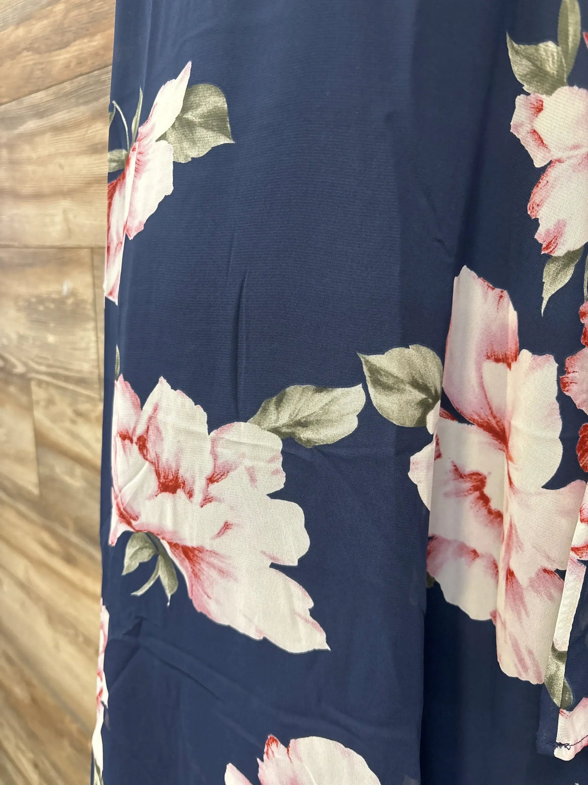 Close-up side view of Hello Miz floral V-neck maternity dress showing large pink-and-white flowers on navy fabric with wood floor background