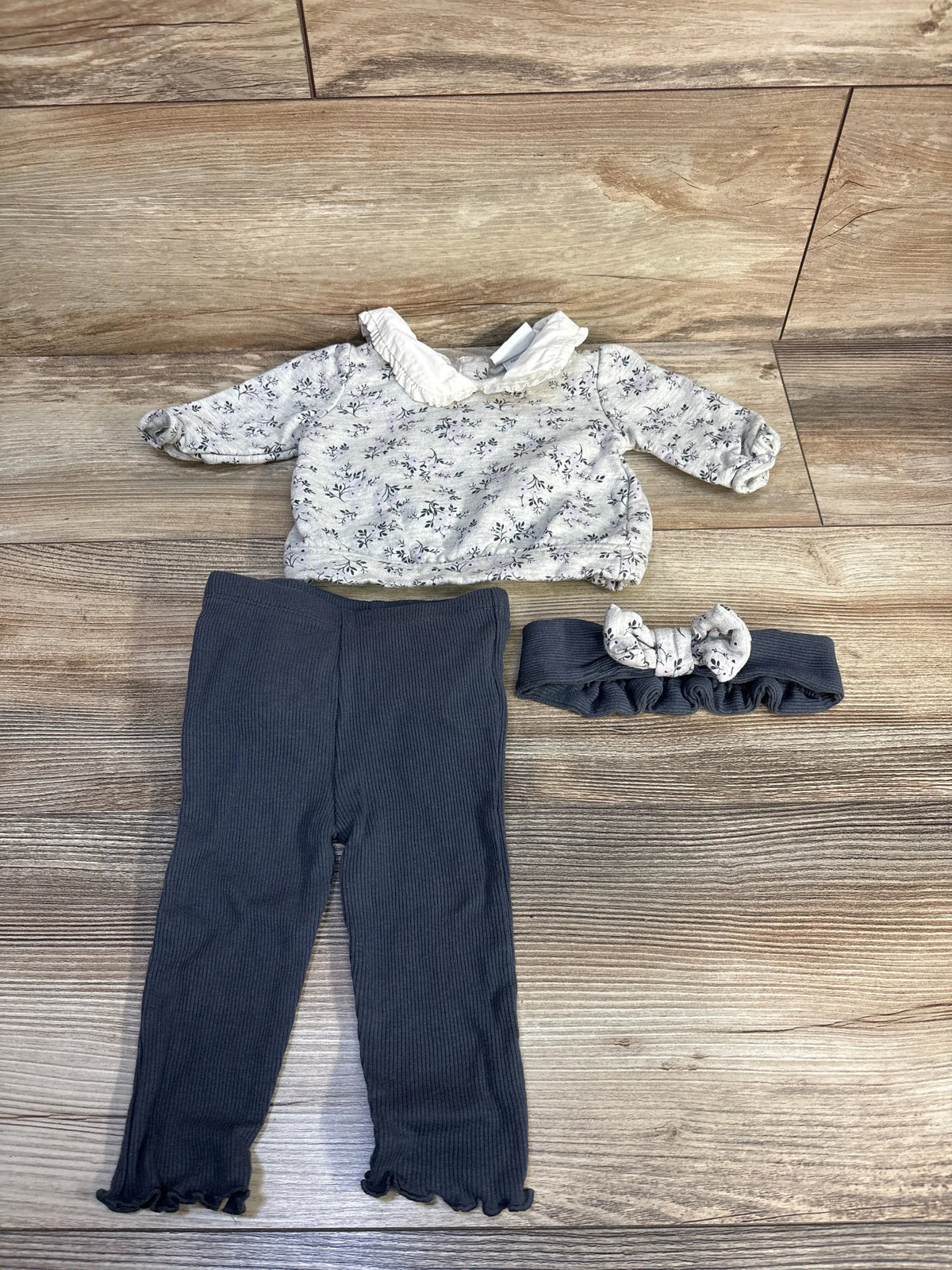 Flat lay of Nicole Miller baby set with floral sweatshirt, ribbed leggings, and matching headband on wood floor