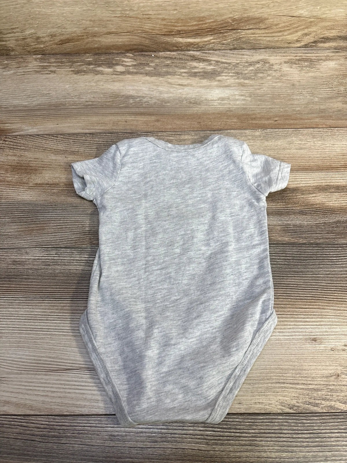 Back view of grey Nike Just Do It bodysuit in size 6M with short sleeves on a wood background