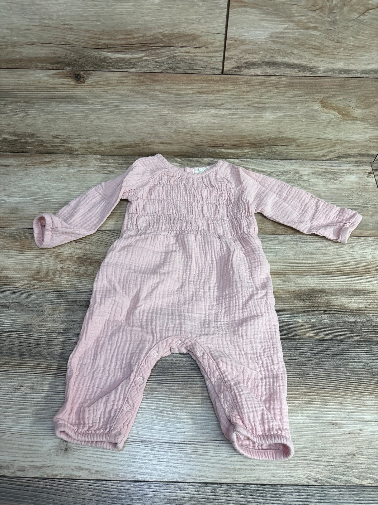 Pink long-sleeve baby romper with snaps, textured cotton, laid on wood floor