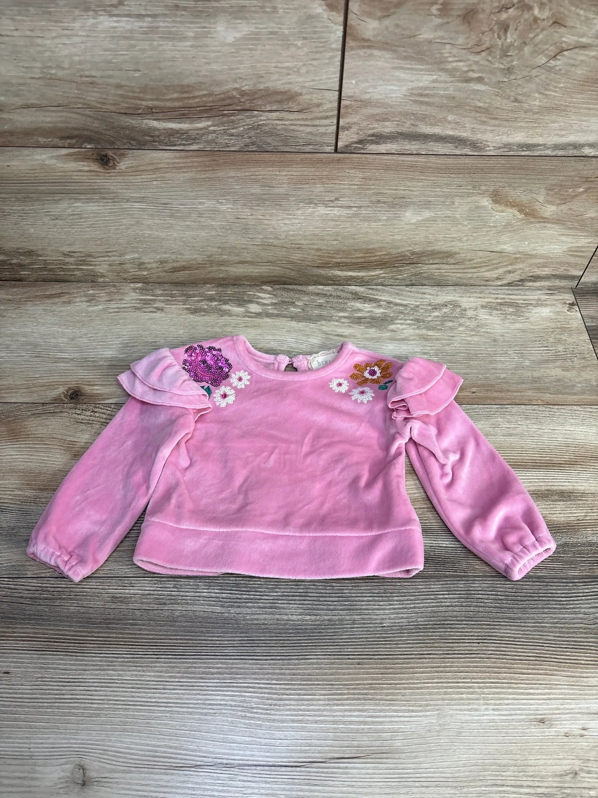 Pink toddler long sleeve shirt with ruffle shoulders and floral embroidery on wood floor