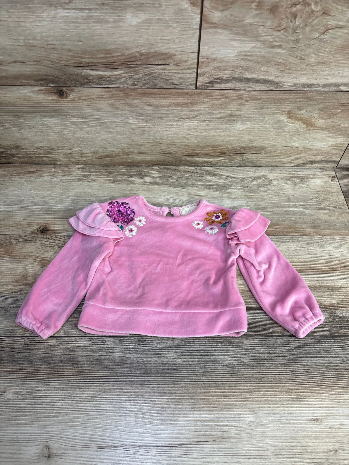 Pink toddler long sleeve shirt with ruffle shoulders and floral embroidery on wood floor