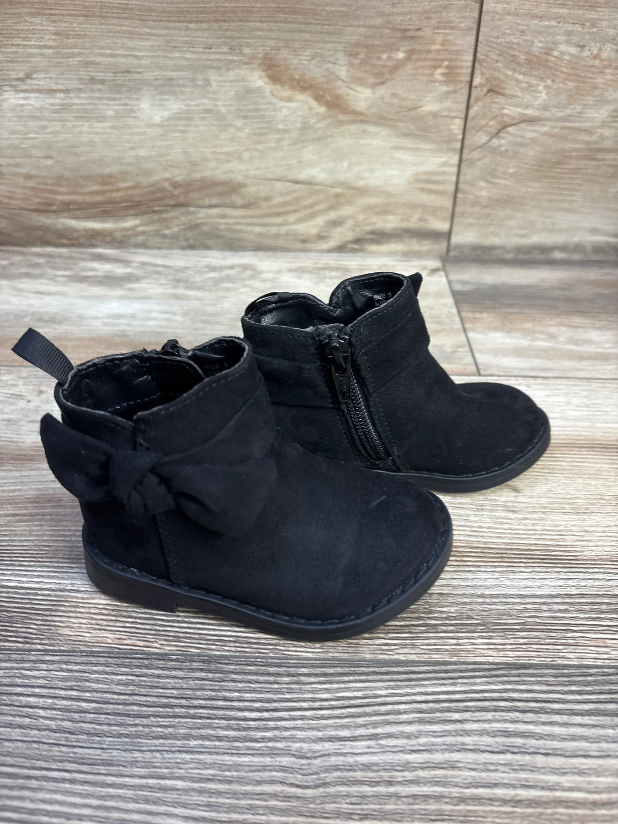 Three-quarter view of Baby Gap black bow ankle boots size 5C showcasing side zipper and back bow on wood floor
