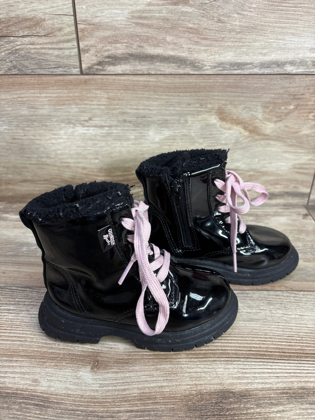 Pair of black shiny OshKosh B'gosh kids boots with pink laces on wooden floor