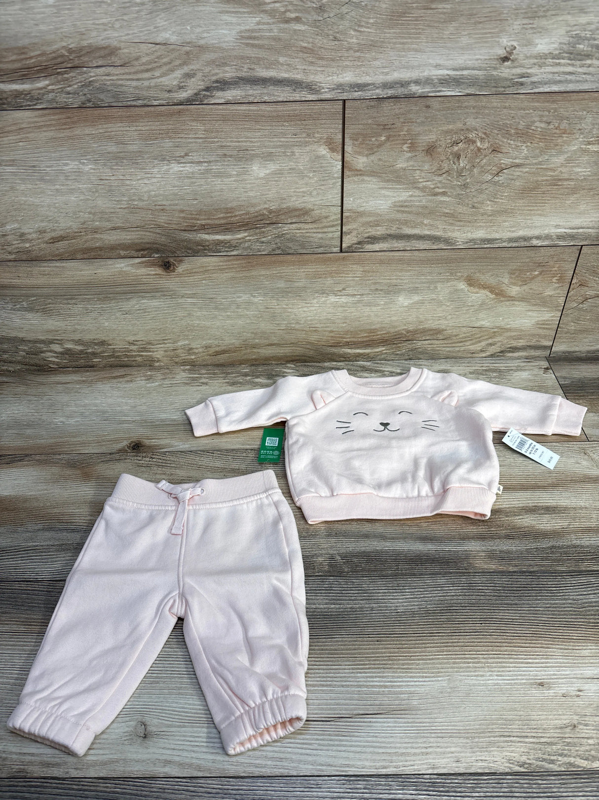 Light pink baby outfit set with cat face sweatshirt and matching pants on wood floor