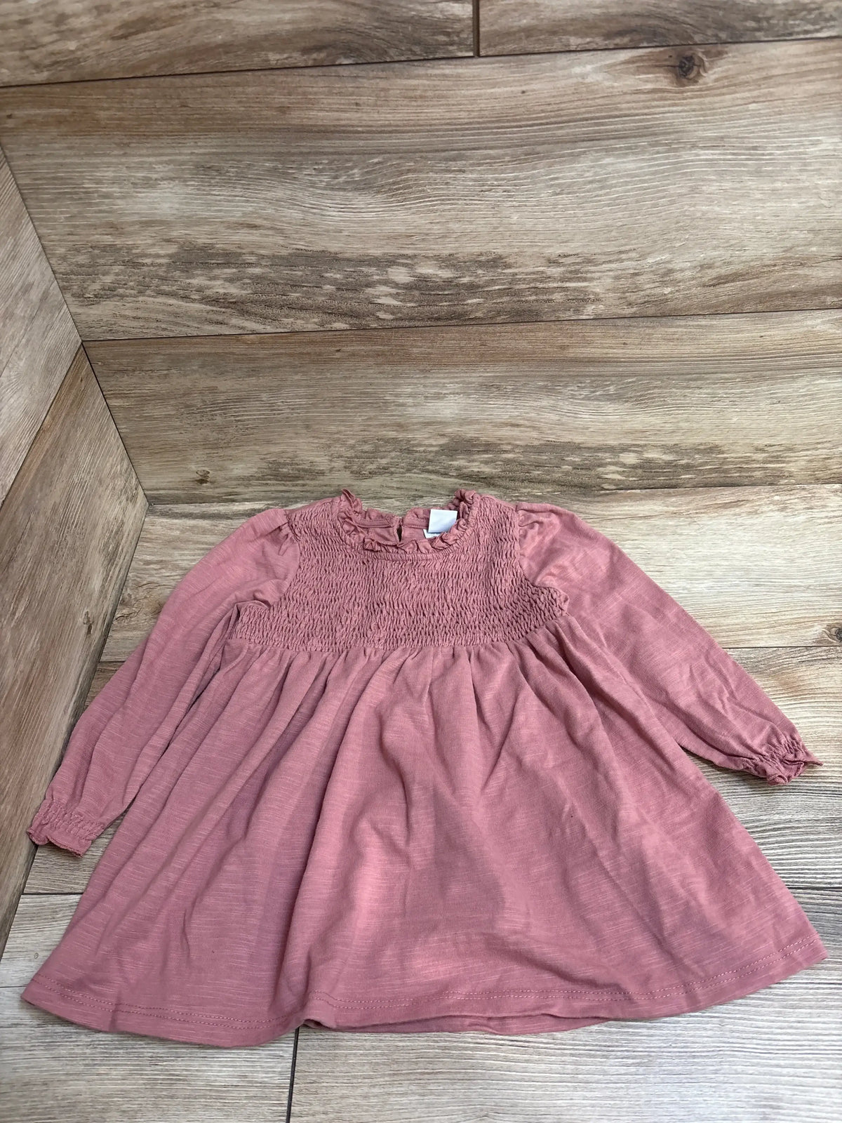 Pink long-sleeve baby dress with smocked bodice on wood floor background