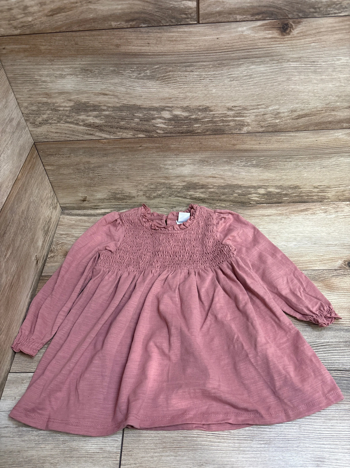 Pink long-sleeve baby dress with smocked bodice on wood floor background