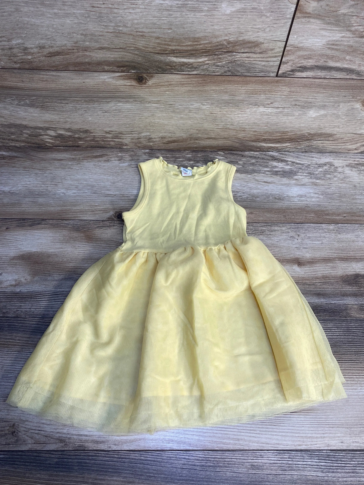 Light yellow sleeveless girls dress with tulle skirt on wooden background