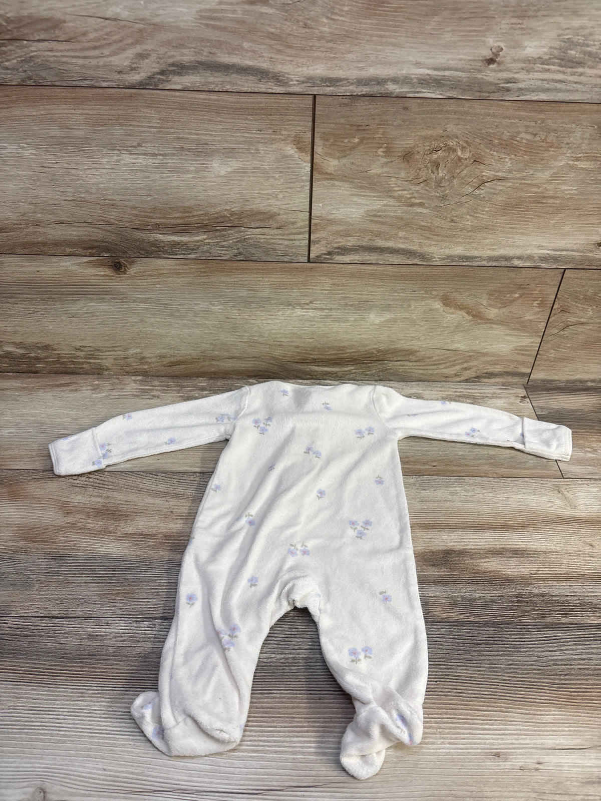 Top view of Carters cream terry cloth sleeper showcasing long sleeves, footed legs, and floral print on a wood floor