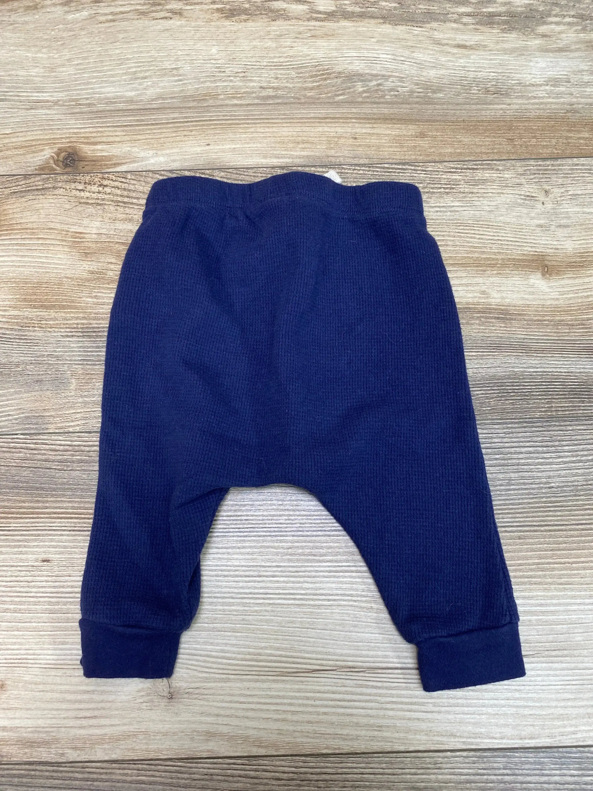 Flat lay of navy baby thermal harem pants (3-6 months) showing ribbed cuffs and drop-crotch thermal knit on light wood background