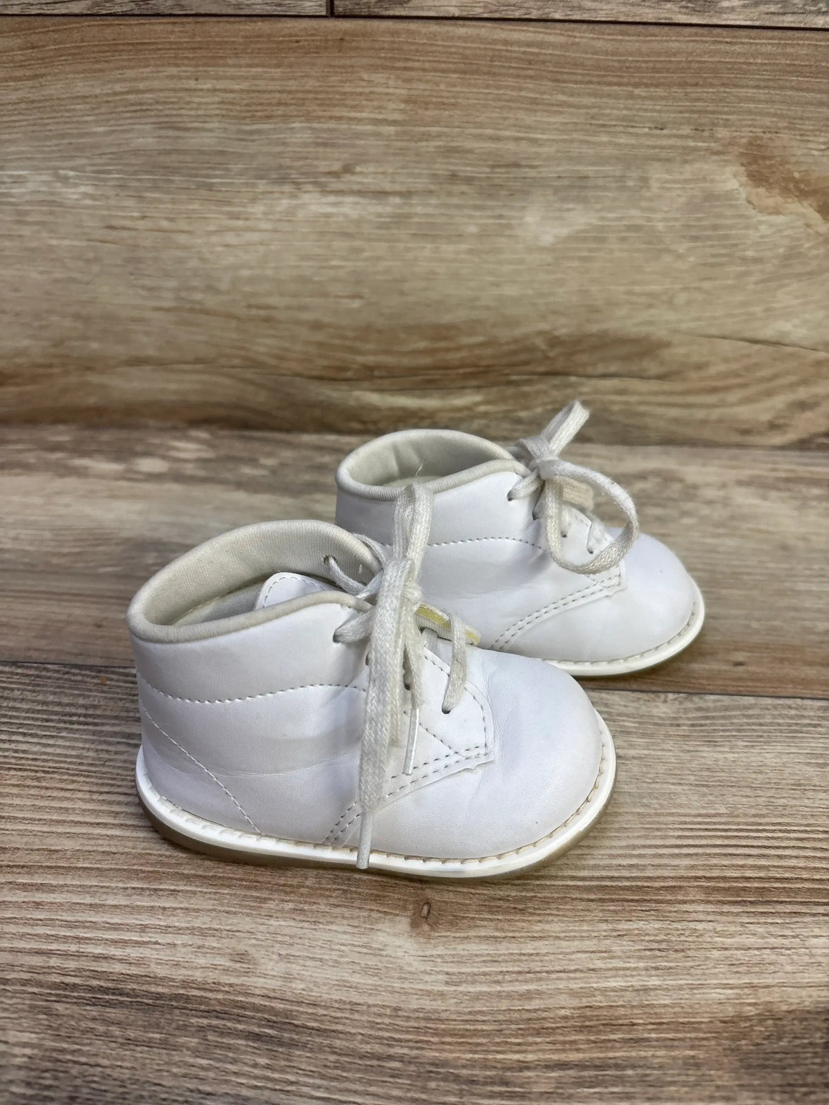 Three-quarter view of Teeny Toes white first-walker baby shoes showing lace-up front, padded collar, and stitched sole on wood background