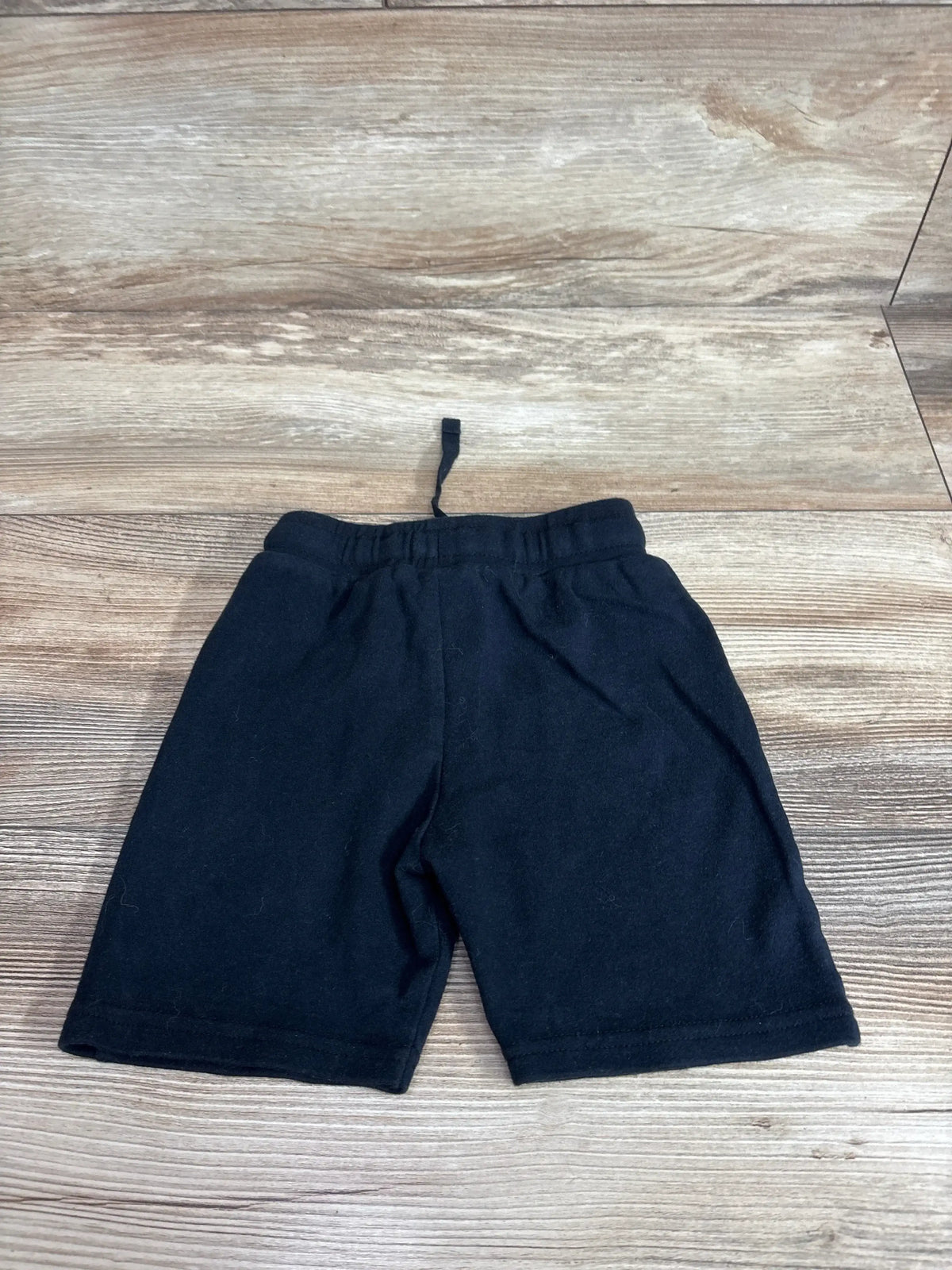 Flat lay of black Moschino baby shorts showcasing elastic waistband and drawstring on light wood background