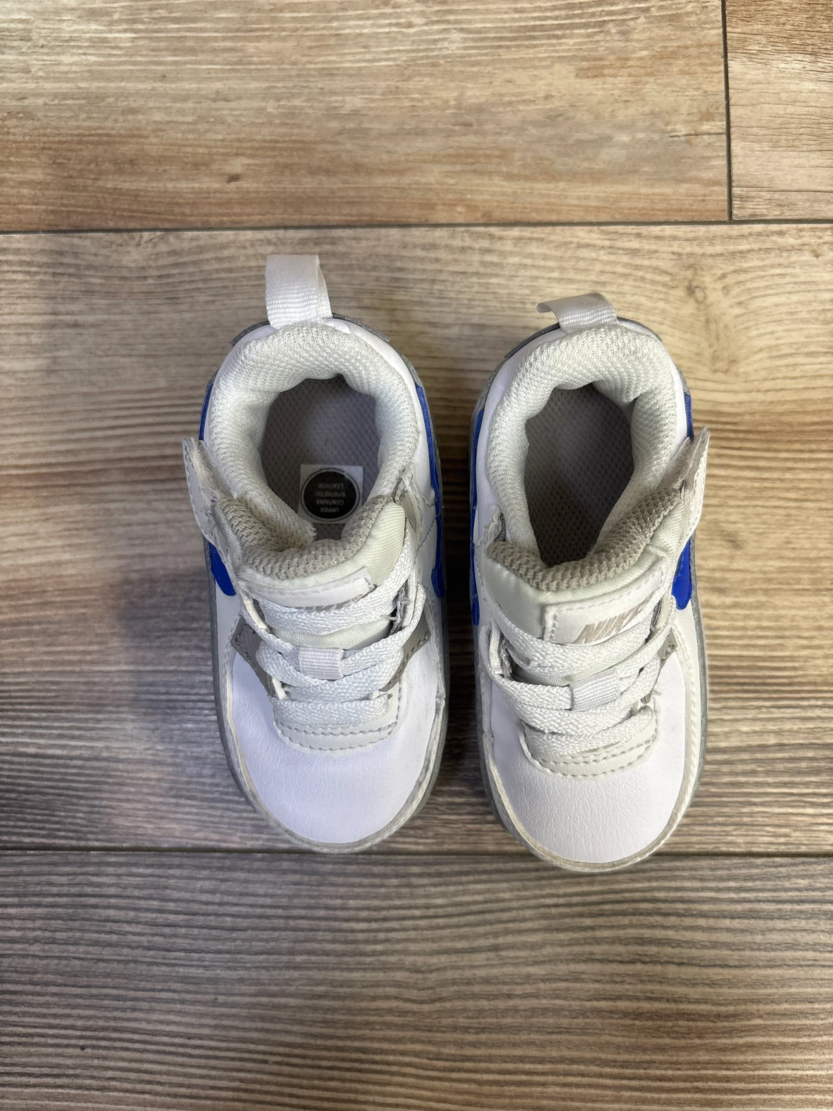 Top-down view of toddler Nike Air Max 90 EasyOn sneakers showcasing Velcro strap, blue Swoosh, and heel pull tab on light wood floor