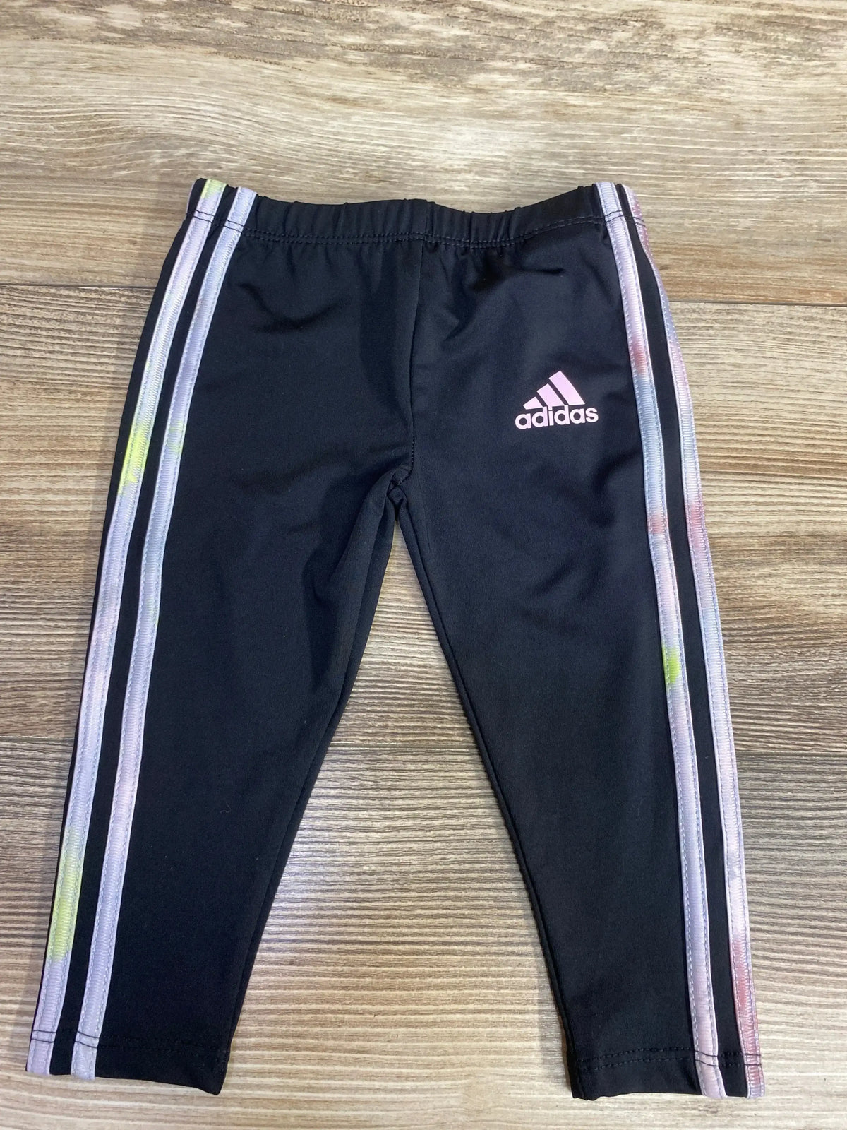 Black Adidas leggings with pink logo and tie-dye three stripes on sides on wooden floor