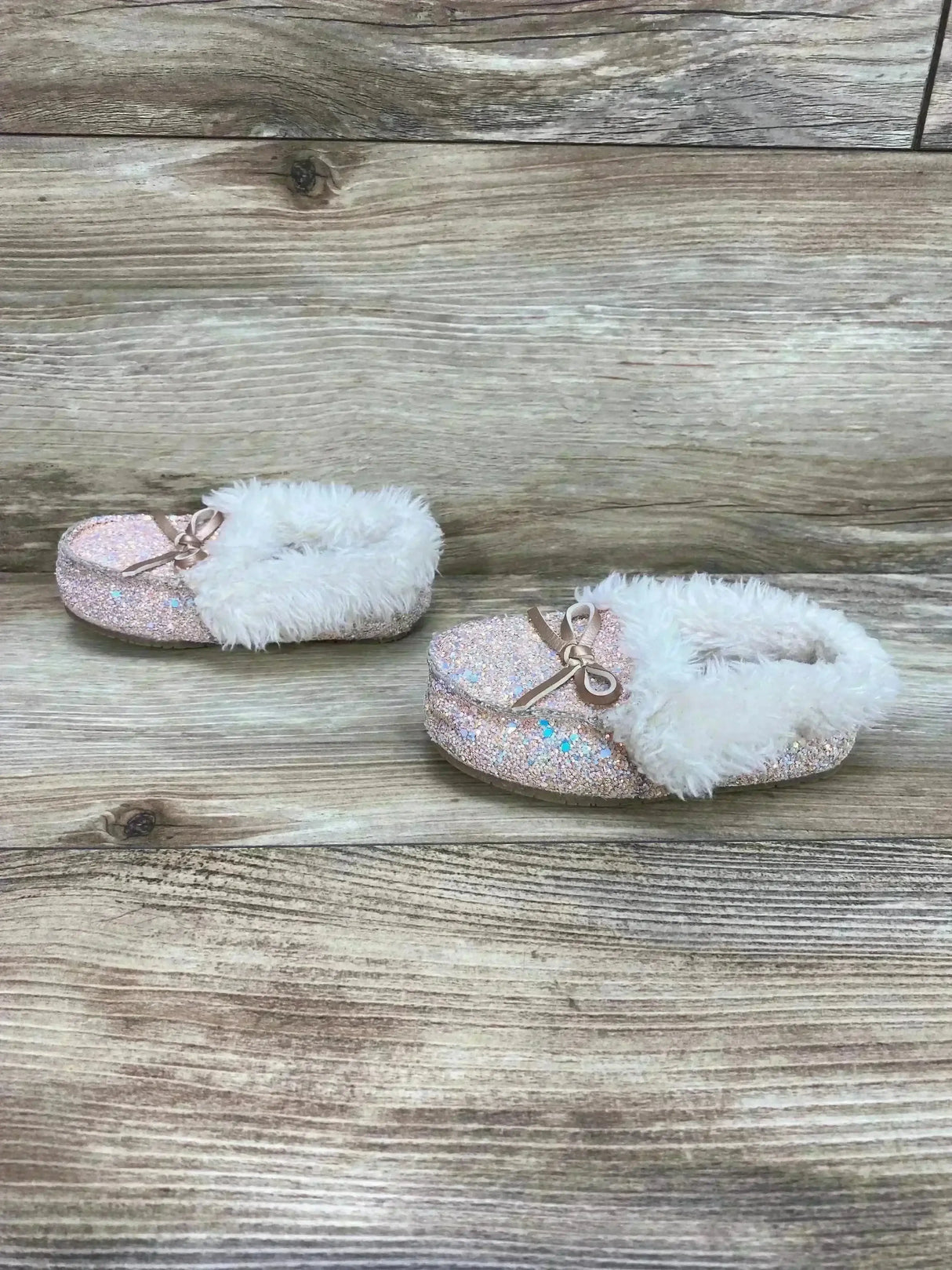 Front angle of Cat & Jack Medora toddler slippers (size 6C) showing pink glitter upper, white faux-fur collar and bow on wood background