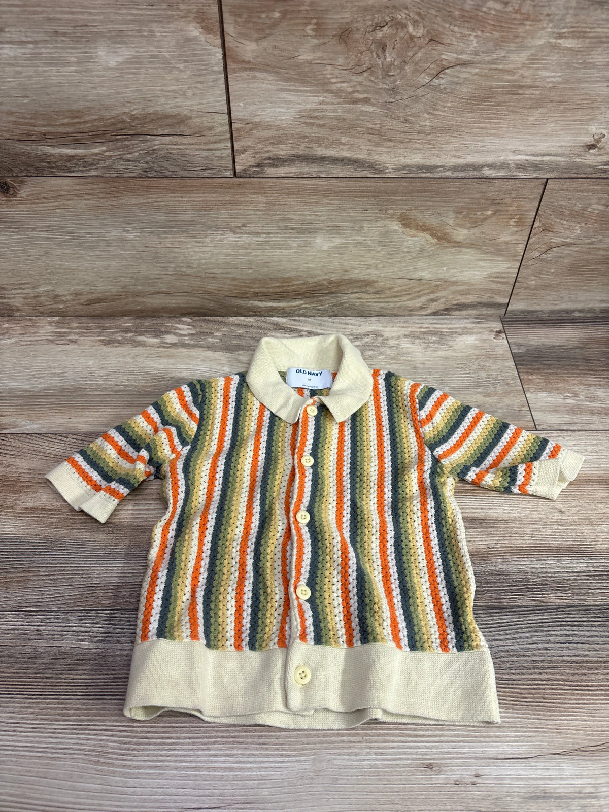 Front view of Old Navy sweater-knit shirt, size 3T, with cream trim, multicolor stripes, and buttons on wood floor