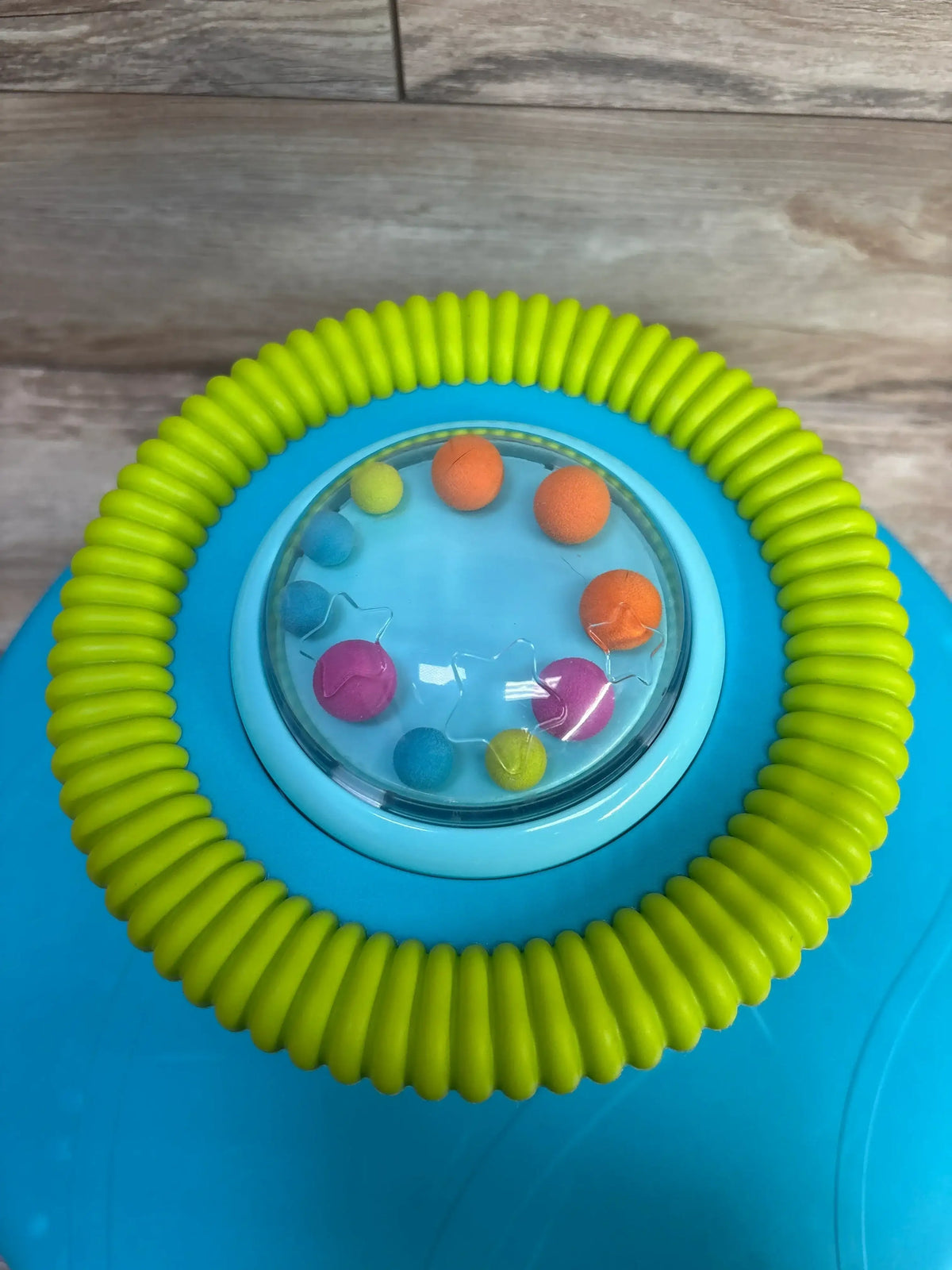 Top view of B. Toys Twirly Time spinning activity toy showcasing colorful bead popper under clear dome and textured green ring on blue base