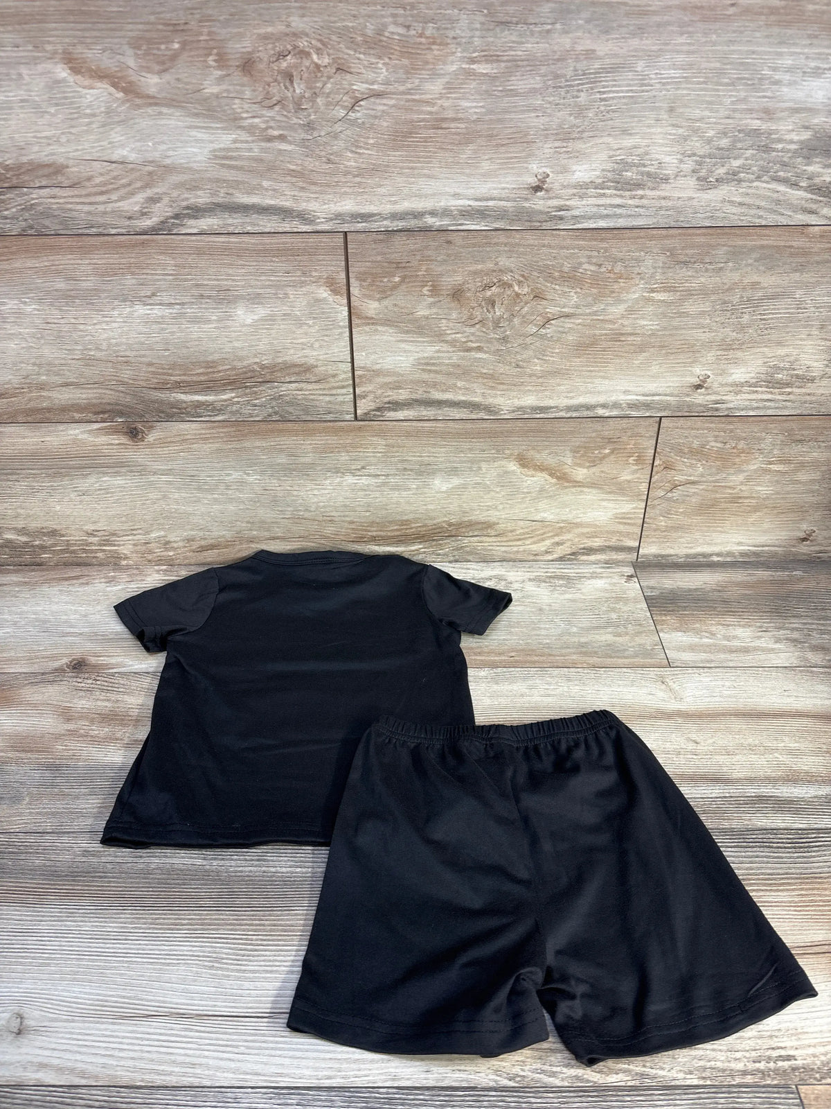 Back view of black toddler two-piece shirt and shorts set showcasing short sleeves and elastic waistband on wood-look floor