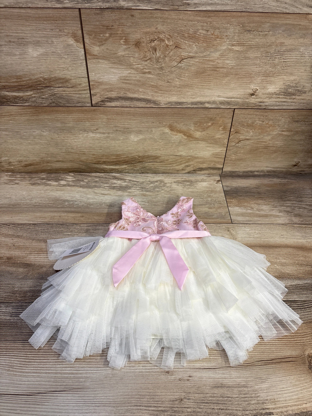 Front of 2-piece baby dress and bloomers showing gold-embroidered pink bodice, ivory tulle skirt, pink bow on wood background