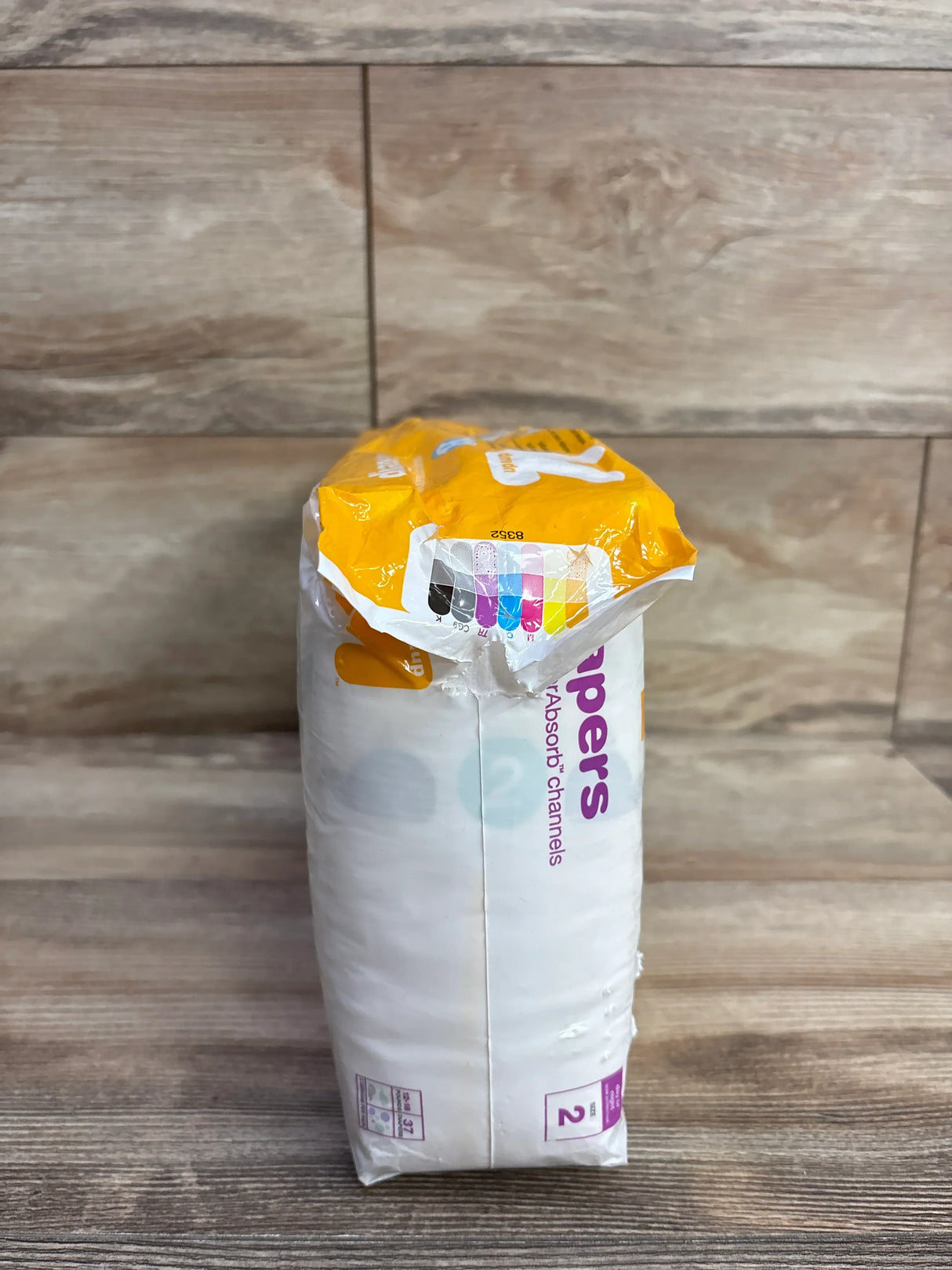 Package of Pampers baby diapers size 2 with yellow and white packaging on wooden surface