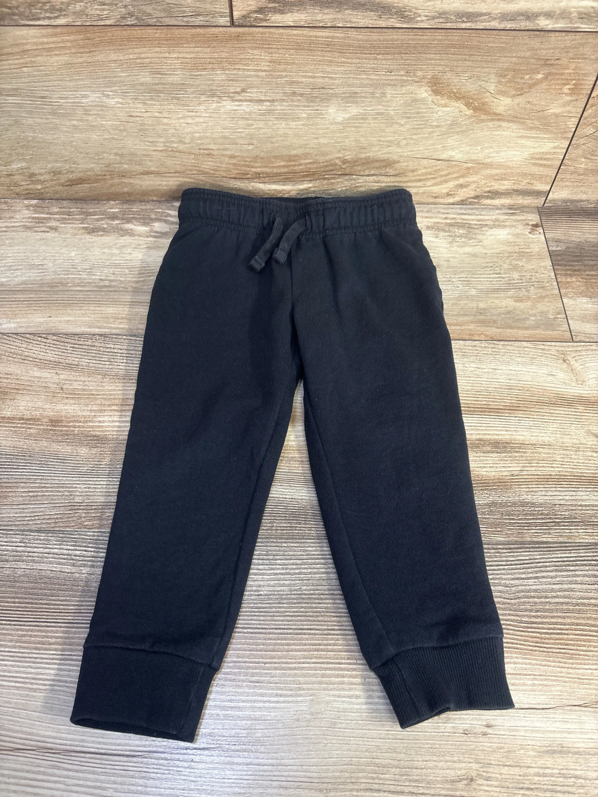 Front view of Carter’s black pull-on drawstring joggers, size 3T, showcasing pockets and ribbed cuffs on wood floor