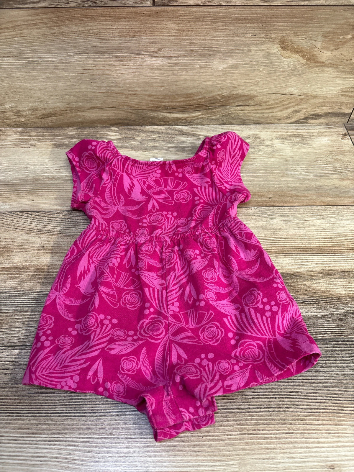Flat lay of Baby Gap shortie romper showing bright pink floral print, elasticized waist and cap sleeves on wood background
