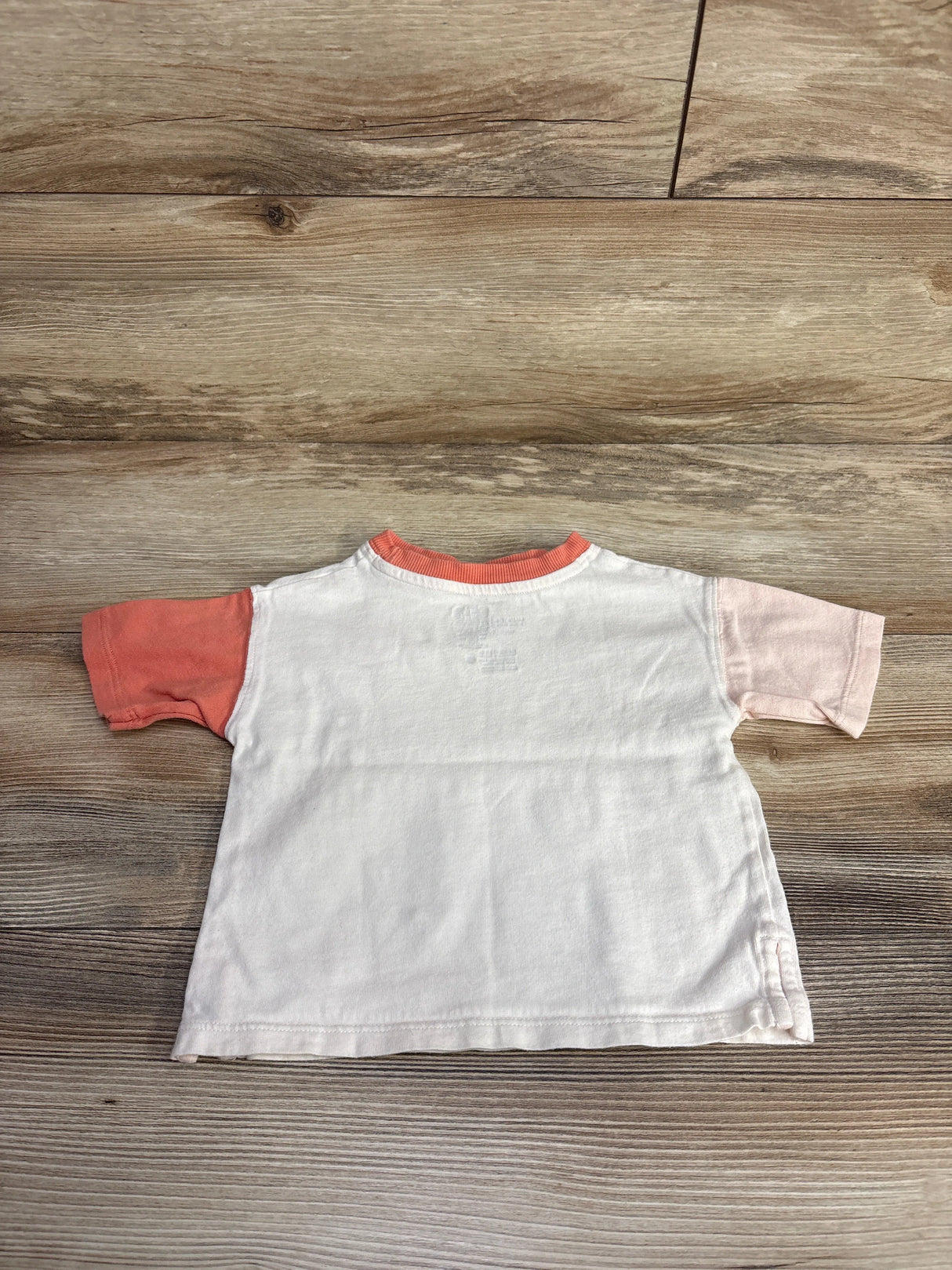 Back view of a short-sleeve toddler T-shirt with one coral and one light pink sleeve on wooden floor