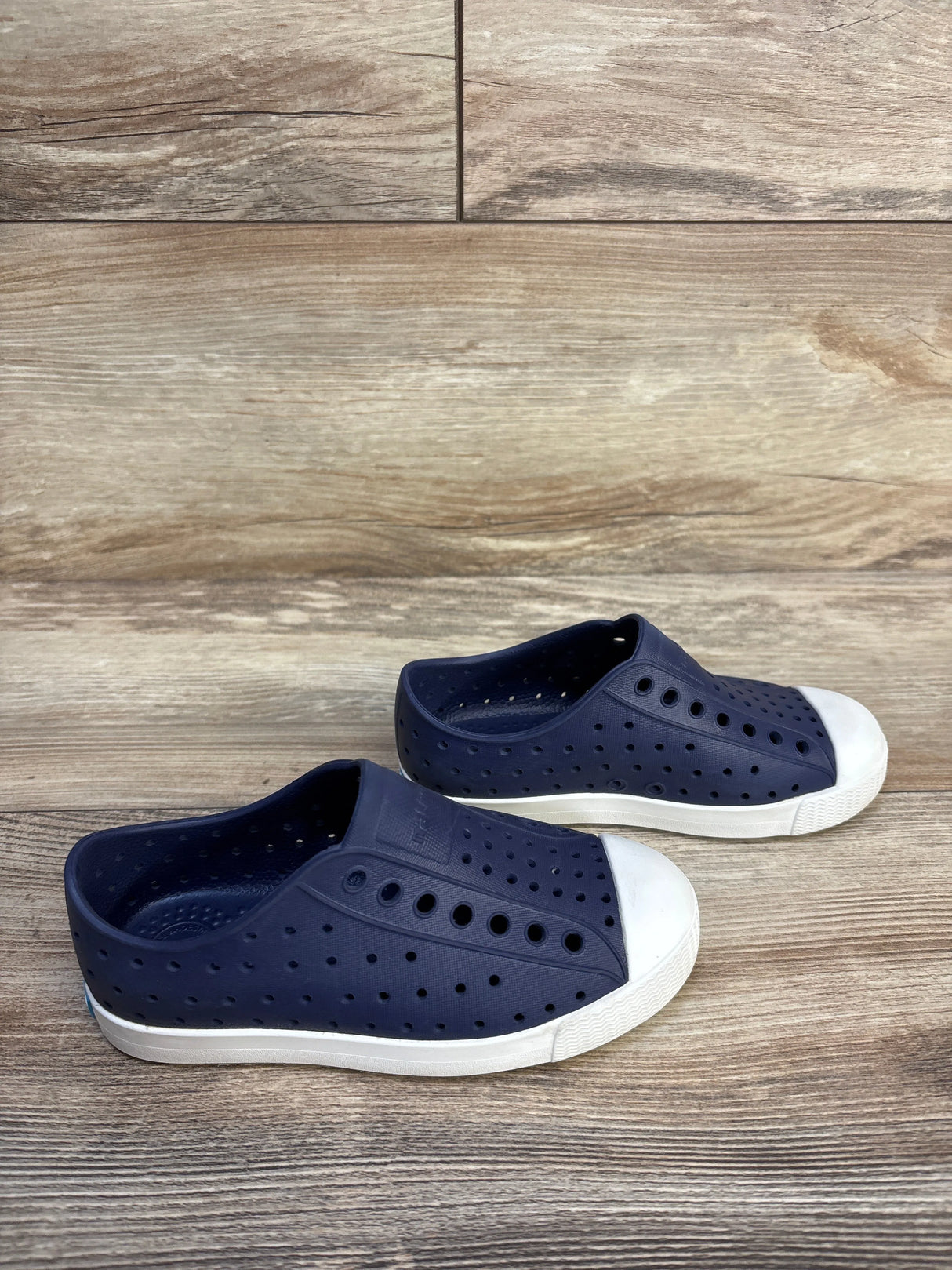 Navy blue slip-on kids shoes with white toe caps and ventilated holes on wood background