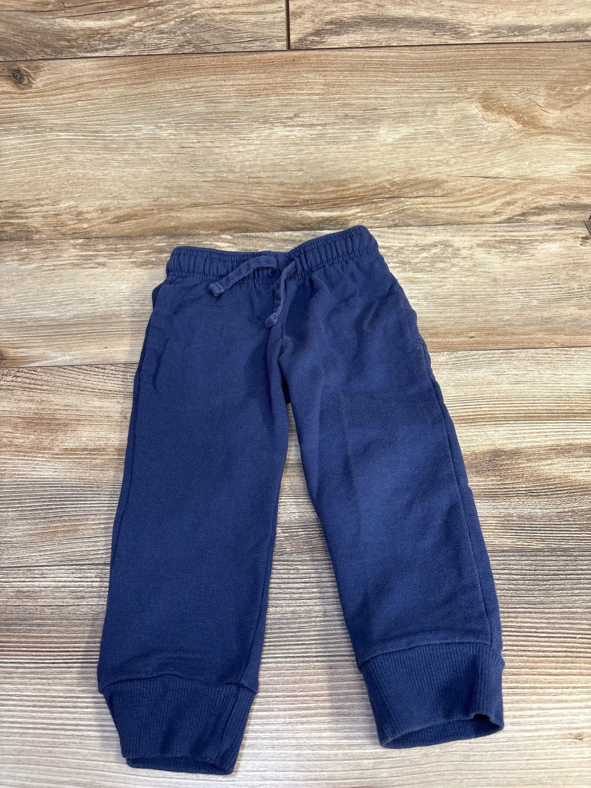 Flat lay of navy toddler drawstring jogger pants showing elastic waistband with drawstring, cuffed ankles, and side pockets on wood background
