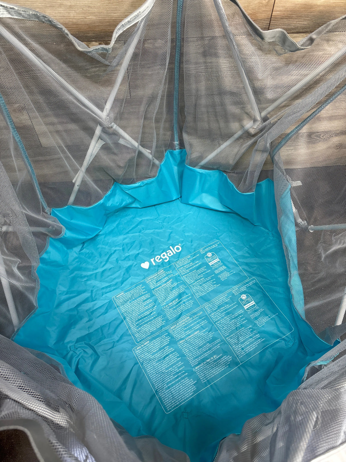 Regalo blue mesh play yard with instruction label, indoor wood floor background