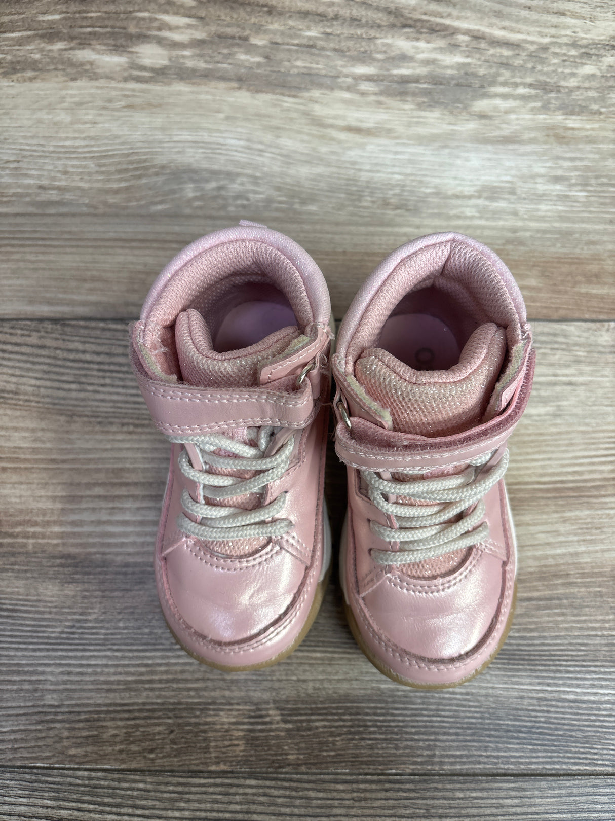 Pair of pink toddler sneakers with white laces and velcro straps on a wooden floor