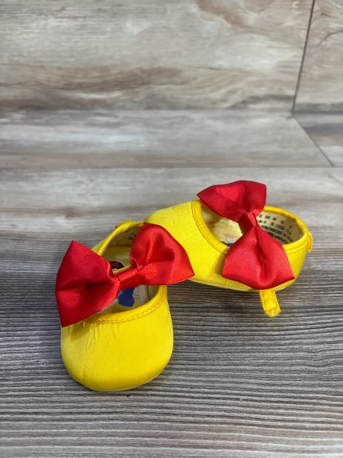 Front and side view of Disney Baby Snow White soft sole shoes in yellow with red bows and pull tabs