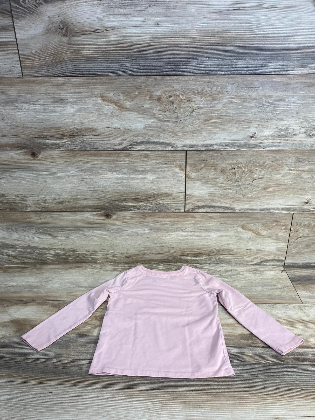 Light pink long sleeve toddler shirt displayed on wooden floor background