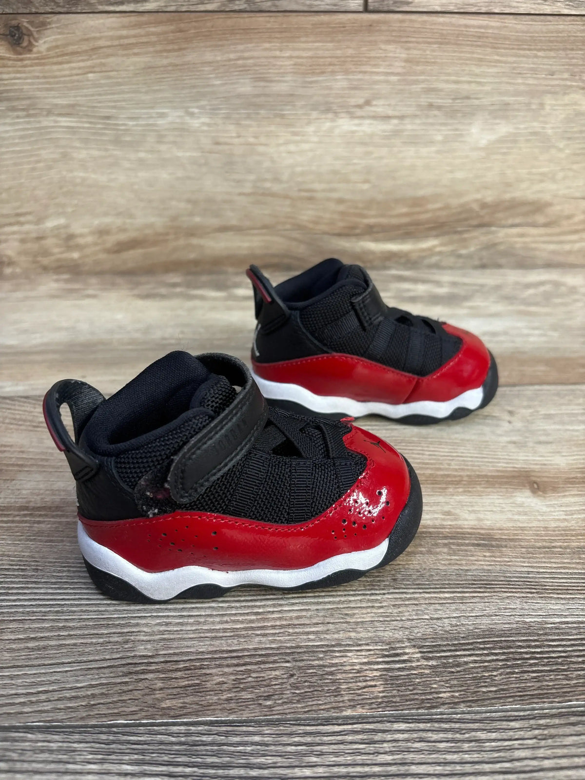 Three-quarter view of Jordan 6 Rings TD Fitness Red sneakers showcasing black mesh upper red patent overlay and white midsole on wood plank floor