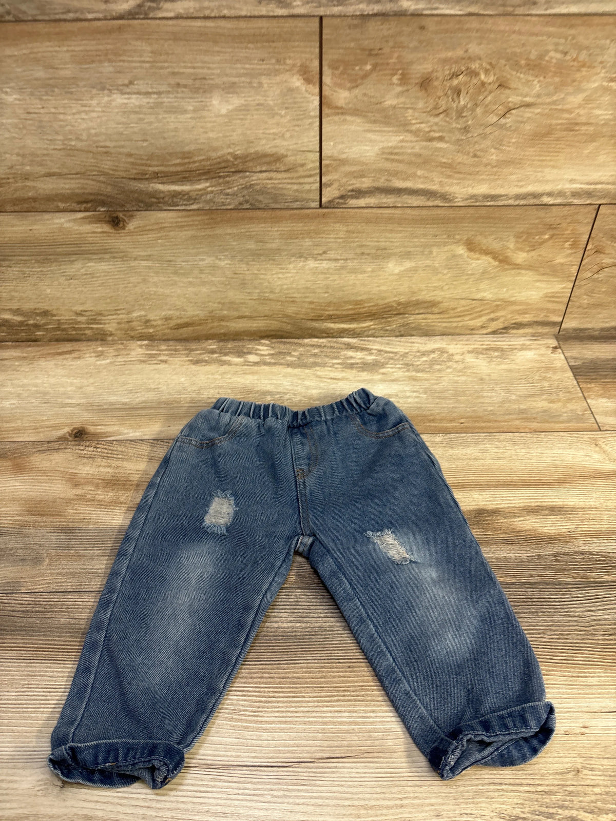 Flat lay of baby pull-on jeans size 9-12 months with elastic waistband, distressed knees and rolled cuffs on wood background